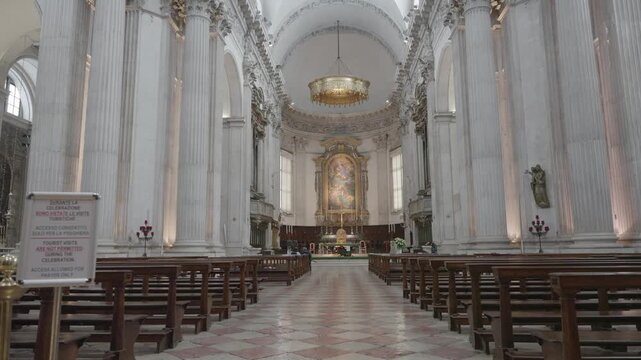 An Interior View Of The Magnificent White Marble Cathedral Nave Featuring Rows Of Wooden Pews Along The Central Aisle And A Golden Baroque Altar Beneath A Large Chandelier, Brescia - Italy