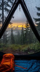 View from inside a tent with rain droplets on the window overlooking a forest and city lights at dusk with an orange backpack on a blue sleeping bag