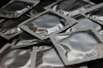 Many sealed silver condom packets scattered across a dark surface.