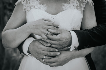 Close-up of intertwined hands of a couple, showcasing wedding rings and delicate lace details of a...