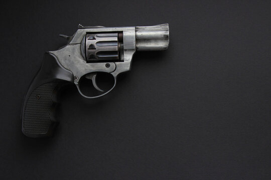 Steel revolver placed to the left on black background, large negative space for text or design.