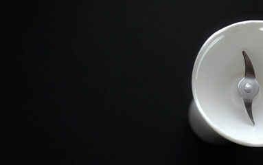 Minimal overhead view of a white chopper cup with stainless-steel blade against a black background.