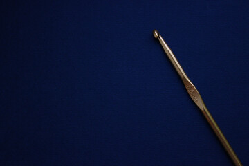 Golden 6.0 mm crochet hook placed diagonally on a dark blue textile background with copy space.