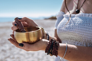 Close up woman begins to play Tibetan bowl with wooden mallet, representing sound healing and meditative focus. Concept of energy of mindfulness and the soothing vibration of inner calm