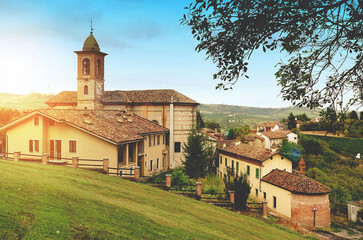 Scenic hilltop village in Piedmont, with church and bell tower surrounded by lush greenery on a bright day.