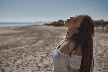 Young 20s serene woman enjoy warmth and sunny weather with eyes closed stands alone on shoreline, feeling free and happy. Relaxation, summer pleasure outdoors concept