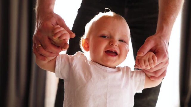 Joyful child takes his first steps with his dad's help, close-up