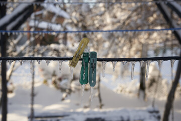 clothespins on a rope covered with ice and icicles, Black clothesline and clothespins, completely covered with a thick layer of ice and icicles, hanging down
