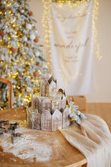 Gingerbread village cake decorated with lights and festive Christmas tree in background