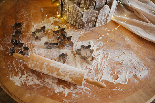 Cookie cutters and rolling pin on flour dusted wooden table, preparation for baking.