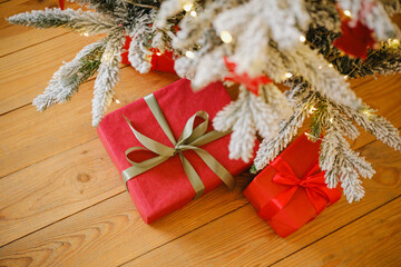 Red holiday gifts under a snowy evergreen tree with warm lights on wood floor