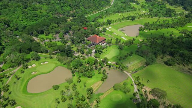 A wider aerial shot of the country club showing the clubhouse, fairways, and water features with drifting clouds casting shadows in Calamba Laguna, Philippines