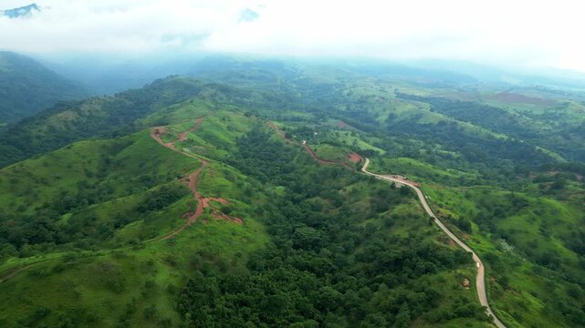 A wide aerial showcasing winding dirt and roads cutting through green mountains, extending across valleys and layered hills under cloudy skies in Quinawan mountain view, Mariveles Bataan, Philippines