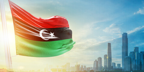 Libya flag wavering in beautiful clouds with building skyline. The flag with drone shot in...