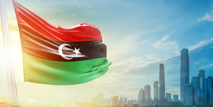 Libya flag wavering in beautiful clouds with building skyline. The flag with drone shot in beautiful sky. Libya national day flag for independence day.