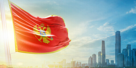 Montenegro flag wavering in beautiful clouds with building skyline. The flag with drone shot in...