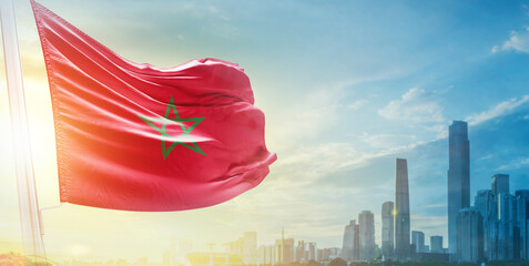 Morocco flag wavering in beautiful clouds with building skyline. The flag with drone shot in beautiful sky. Morocco national day flag for independence day.