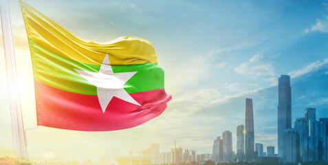 Myanmar (Burma) flag wavering in beautiful clouds with building skyline. The flag with drone shot in beautiful sky. Myanmar Burma national day flag for independence day.