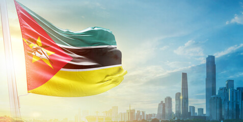 Mozambique flag wavering in beautiful clouds with building skyline. The flag with drone shot in beautiful sky. Mozambique national day flag for independence day.