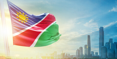 Namibia flag wavering in beautiful clouds with building skyline. The flag with drone shot in beautiful sky. Namibia national day flag for independence day.