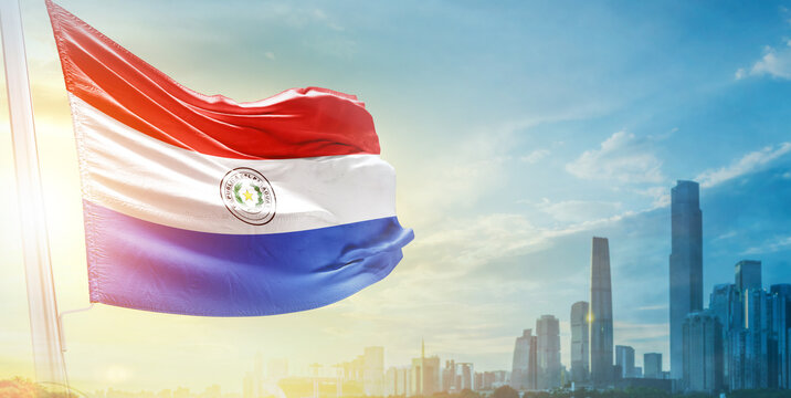 Paraguay flag wavering in beautiful clouds with building skyline. The flag with drone shot in beautiful sky. Paraguay national day flag for independence day. - Powered by Adobe