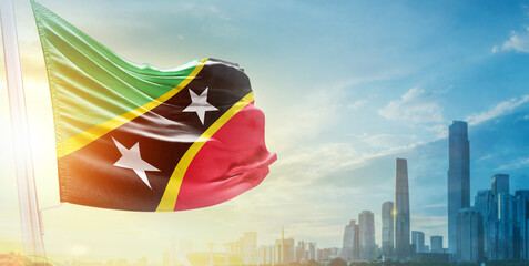 Saint Kitts and Nevis flag wavering in beautiful clouds with building skyline. The flag with drone...