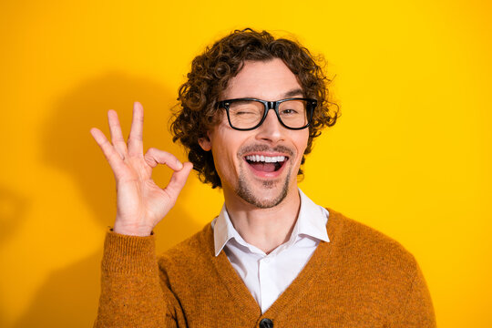 Happy stylish man with glasses in a mustard cardigan makes ok sign against yellow background for friendly business lifestyle advertising photo - Powered by Adobe