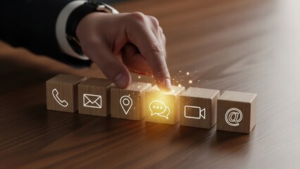 Hand selecting a glowing communication icon on wooden blocks.