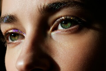 Close-up of a person's face with glittery eye makeup highlighting green eyes and detailed facial features