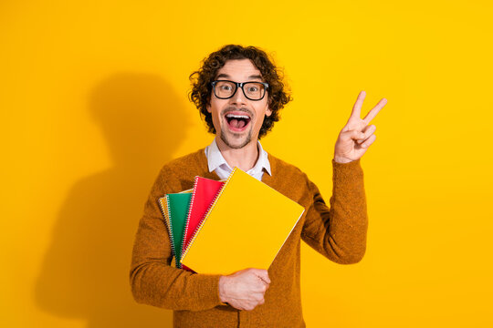 Happy young man with curly hair wearing glasses cardigan holds colorful notebooks against a bright yellow background in a promotional lifestyle scene