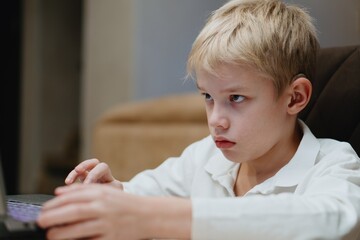 A 9-year-old boy with hearing aids plays on a laptop, fully engaged. Natural, authentic moment of modern childhood and inclusive digital play
