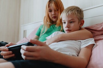 A 9-year-old boy with hearing aids plays naturally with his 12-year-old sister. Authentic sibling moment showcasing inclusive family bonds across age differences