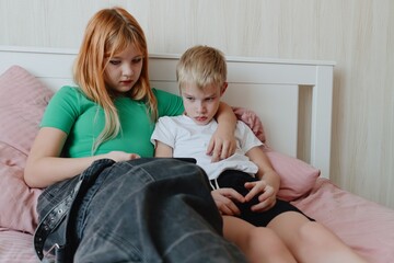 A 9-year-old boy with hearing aids plays naturally with his 12-year-old sister. Authentic sibling moment showcasing inclusive family bonds across age differences