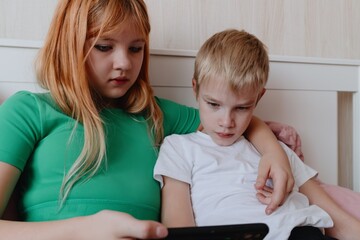 A 9-year-old boy with hearing aids plays naturally with his 12-year-old sister. Authentic sibling moment showcasing inclusive family bonds across age differences