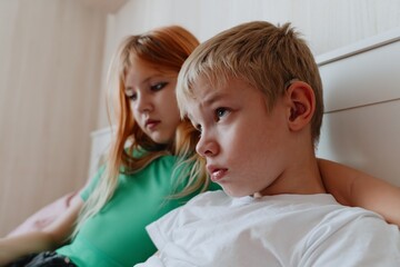 A 9-year-old boy with hearing aids plays naturally with his 12-year-old sister. Authentic sibling moment showcasing inclusive family bonds across age differences