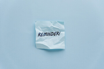 Crumpled reminder note on a light blue background. The note has the word 'REMINDER ' written in bold black letters.