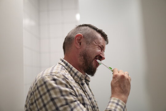 Man squinting eyes brushing teeth during morning routine