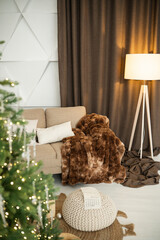 Naklejka premium Warm living room corner with sofa, plush blanket, floor lamp and Christmas tree