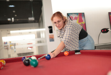 Woman playing pool aiming cue stick on red table