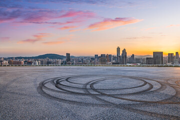 Naklejka premium Asphalt road ground with tire tracks and city skyline at sunset