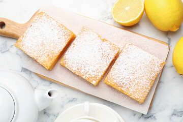 Tasty lemon bars with powdered sugar and fresh fruits on white marble table, flat lay