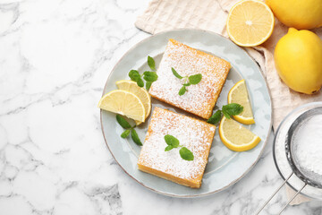 Tasty lemon bars with powdered sugar, mint and fresh fruits on white marble table, flat lay. Space for text
