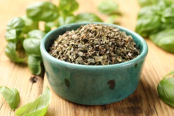 Dry basil in bowl and fresh green leaves on wooden table, closeup