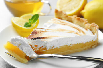 Slice of tasty lemon meringue tart with mint served on light grey table, closeup