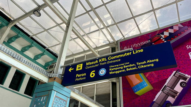 A sign for the train KRL Commuter Line hangs above a building. The sign is blue and white and has the numbers 6 and 6 on it