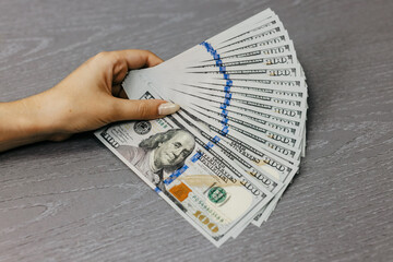 Hand holding a fan of hundred dollar bills on a wooden surface, showcasing wealth and financial...