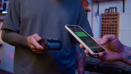 Cropped shot of hand of unrecognizable male customer using contactless payment by his smartphone in modern tattoo parlor - Powered by Adobe