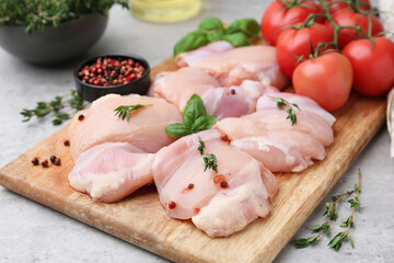 Raw chicken thighs with herbs, peppercorns and tomatoes on light table, closeup