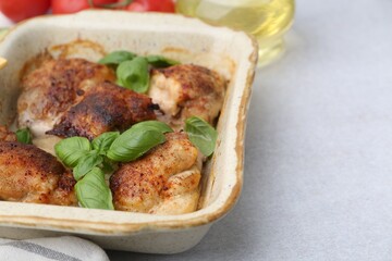 Tasty cooked chicken thighs with basil in baking dish and ingredients on light grey table, closeup. Space for text