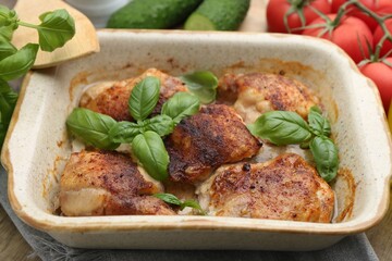 Tasty cooked chicken thighs with basil in baking dish and ingredients on table, closeup